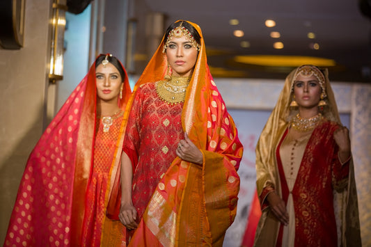 Models showcasing traditional Indian ethnic wear with rich red and gold sarees and ornate jewelry during a festive fashion show.