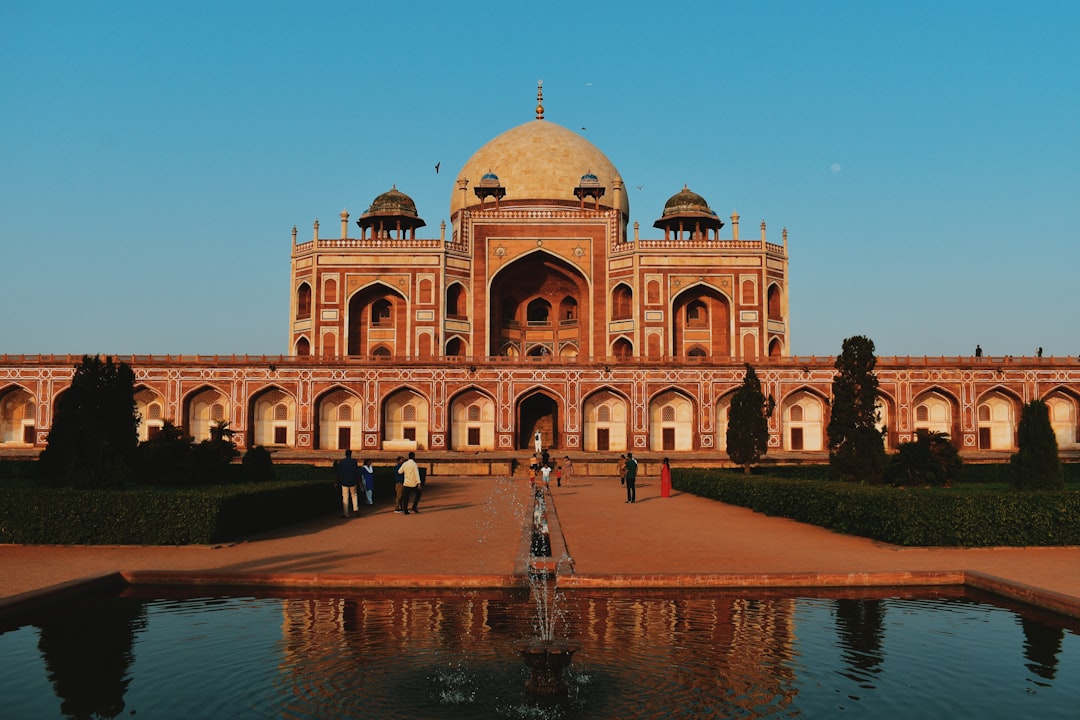 A large, symmetrical Moghul-era tomb (Humayun's Tomb) made of red sandstone with a central dome, reflected in a foreground pool and fountain.